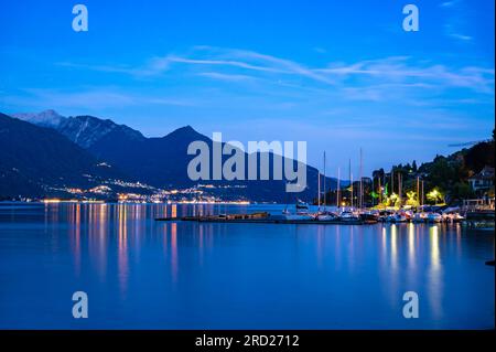 Die Stadt Pianello del lario, am Comer See, und die Promenade am See, in der Abenddämmerung. Alpen, Berge und Seestädte in der Ferne. Stockfoto