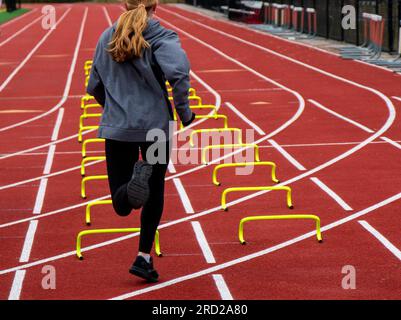 Rückansicht einer Läuferin, die auf einer Strecke über gelbe Minihürden in der Spur fährt. Stockfoto
