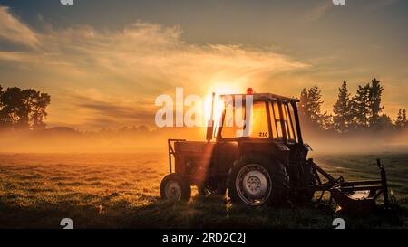 Nebeliger Sonnenaufgang über einem alten Traktor Stockfoto