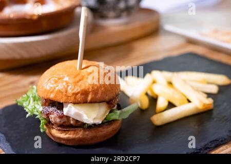 Eine einzelne Tapas-Portion eines kleinen Rinderburgers garniert mit Brie-Käse, serviert mit pommes Frites in einer Tapas-Bar. Stockfoto