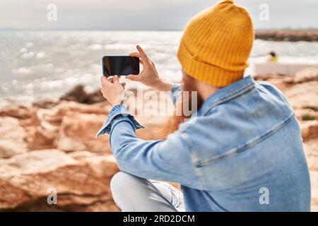 Junge Rotschopf Mann auf der Rückansicht stehen machen Foto mit dem Smartphone am Meer Stockfoto