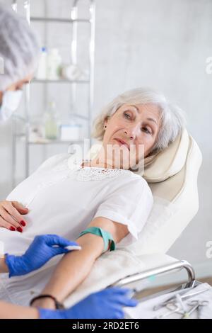 Weibliche Ärztin, die der schläfrigen, müden alten Frau in der Klinik eine Injektion gibt. Stockfoto