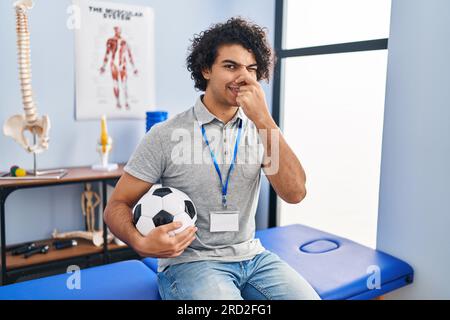 Ein hispanischer Mann mit lockigem Haar, der als Football Physiotherapeutin arbeitet und etwas stinkt und ekelhaft riecht, unerträglicher Geruch, Atemanhalten mit Fangen Stockfoto