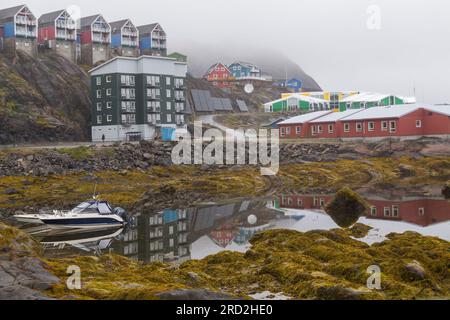 Wohnwohnungen spiegeln sich im Wasser in Maniitsoq (auch bekannt als Sukkertoppen), Westgrönland an einem nebeligen Tag im Juli Stockfoto