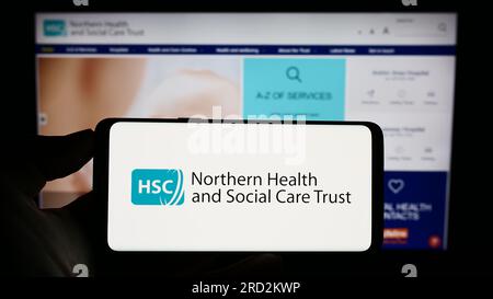 Person, die ein Mobiltelefon mit dem Logo von Health and Social Care (HSC) in Nordirland auf dem Bildschirm vor der Webseite hält. Konzentrieren Sie sich auf das Display des Telefons. Stockfoto