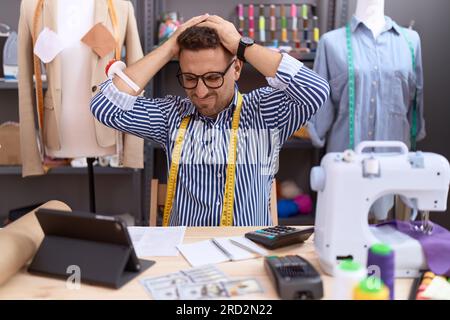 Hispanischer Mann mit Bartschneider-Designer, der im Atelier arbeitet, der verzweifelt und gestresst an Kopfschmerzen leidet, weil er Schmerzen und Migräne hat. Hände auf den Kopf Stockfoto