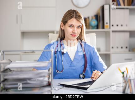 Eine Ärztin, die am Tisch sitzt und in die Kamera schaut Stockfoto