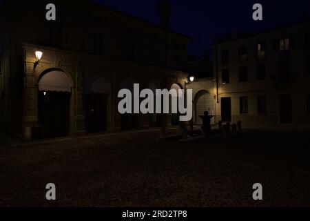 Ein von Lampen beleuchteter Platz mit einem Springbrunnen in der Mitte in einer italienischen Stadt bei Einbruch der Dunkelheit Stockfoto