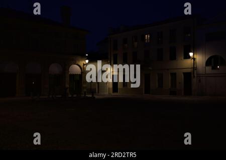 Ein von Lampen beleuchteter Platz mit einem Springbrunnen in der Mitte in einer italienischen Stadt bei Einbruch der Dunkelheit Stockfoto