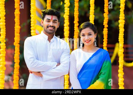 Porträtaufnahme eines glücklichen jungen Paares, das vor dem Blumendekorationshintergrund vor die Kamera schaut - Konzept einer festlichen Feier Stockfoto