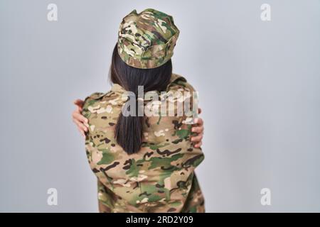 Junge Südasianerin in Tarnuniform, die sich glücklich und positiv umarmt. Selbstliebe und Selbstfürsorge Stockfoto