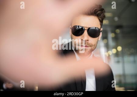 Stop-Geste, Bodyguard in dunkler Sonnenbrille und schwarzer Anzug, der in die Kamera schaut, Halt zeigt, Hotelsicherheit, Sicherheitsmanagement, uniformierter Wachmann im Dienst, Stockfoto