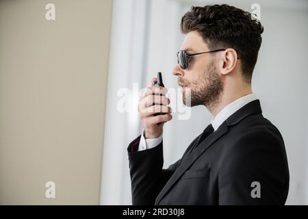 Überwachung, Bodyguard kommuniziert über Walkie-Talkie, Mann mit Sonnenbrille und schwarzem Anzug mit Krawatte, Hotelsicherheit, Sicherheitsmanagement, uniformiertes G. Stockfoto