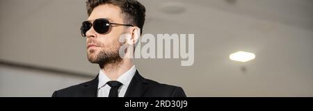 Professionelle Kopfaufnahmen, Bodyguard-Service, gutaussehender Mann mit Sonnenbrille und schwarzem Anzug mit Krawatte, Hotelsicherheit, Sicherheitsmanagement, Überwachung und vig Stockfoto
