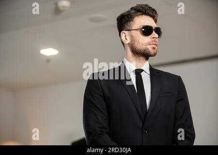 Professionelle Kopfaufnahmen, Bodyguard-Service, gutaussehender Mann mit Sonnenbrille und schwarzem Anzug mit Krawatte, Hotelsicherheit, Sicherheitsmanagement, Überwachung und vig Stockfoto