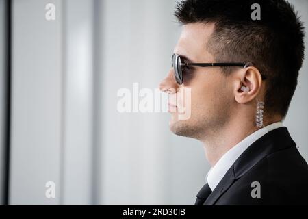 Professionelle Kopfaufnahmen, Bodyguard-Arbeit, Seitenansicht eines gutaussehenden Mannes mit Sonnenbrille und schwarzem Anzug mit Krawatte, Hotelsicherheit, Sicherheitsmanagement, Überwachung Stockfoto