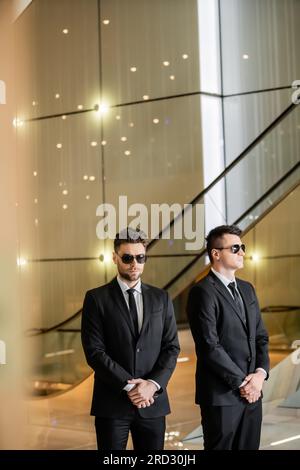 Sicherheitsmanagement des Hotels, zwei gutaussehende Männer in formeller Kleidung und Sonnenbrille, Leibwächter im Dienst, Sicherheitsmaßnahmen, Wachsamkeit, Anzüge und Krawatten, Privat Stockfoto