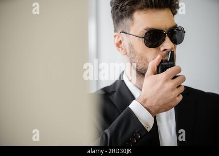 Überwachung, Bodyguard kommuniziert über Walkie-Talkie, Mann in Sonnenbrille und Anzug mit Krawatte, Hotelsicherheit, Sicherheitsmanagement, uniformierter Wachmann Stockfoto