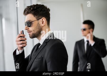 Überwachung, Bodyguard kommuniziert über Walkie-Talkie, Mann mit Sonnenbrille und schwarzem Anzug mit Krawatte, Hotelsicherheit, Sicherheitsmanagement, uniformiertes G. Stockfoto