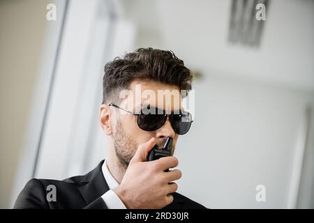 Überwachung, Bodyguard kommuniziert über Walkie-Talkie, Mann mit Sonnenbrille und schwarzem Anzug mit Krawatte, Hotelsicherheit, Sicherheitsmanagement, uniformiertes G. Stockfoto