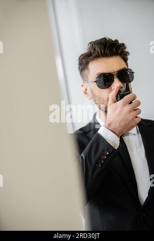 Überwachung, Bodyguard kommuniziert über Walkie-Talkie, Mann mit Sonnenbrille und schwarzem Anzug mit Krawatte, Hotelsicherheit, Sicherheitsmanagement, uniformiertes G. Stockfoto
