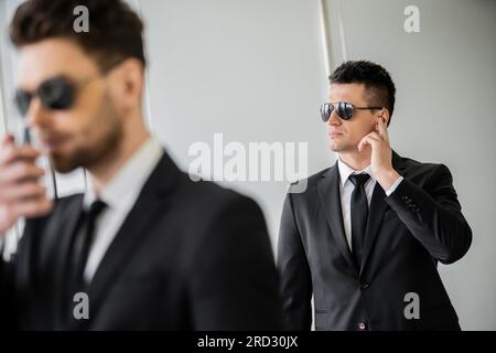 Bodyguard kommuniziert über Ohrhörer, Mann mit Sonnenbrille und schwarzem Anzug mit Krawatte, Hotelsicherheit, Sicherheitsmanagement, Überwachung und Wachsamkeit, wo Stockfoto