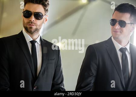Sicherheitsmanagement, zwei gutaussehende Männer in formeller Kleidung und Sonnenbrille, Leibwächter im Dienst, Sicherheitsmaßnahmen, Wachsamkeit, Anzüge und Krawatten, Private Sicherheitsdienste, Stockfoto