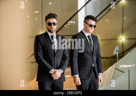 Sicherheitsmanagement eines Luxushotels, zwei gutaussehende Männer in formeller Kleidung und Sonnenbrille, Leibwächter im Dienst, Sicherheitsmaßnahmen, Wachsamkeit, Anzüge und Krawatten, P Stockfoto