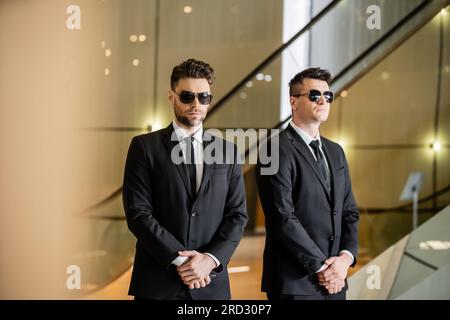 Sicherheitsmanagement eines Luxushotels, zwei gutaussehende Männer in formeller Kleidung und Sonnenbrille, Wachen im Dienst, Sicherheitsmaßnahmen, Wachsamkeit, Anzüge und Krawatten, priva Stockfoto