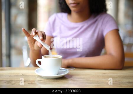 Nahaufnahme einer schwarzen Frau, die Zucker in eine Kaffeetasse auf einer Barterrasse wirft Stockfoto