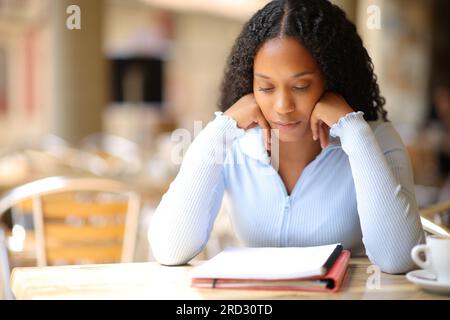 Eine schwarze Frau, die Notizen aus einem Notizbuch auf der Terrasse des Cafés auswendig lernt Stockfoto
