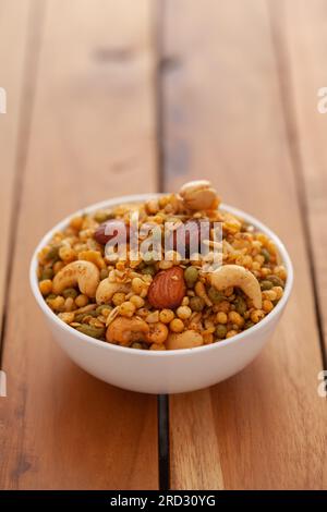 Nahaufnahme der Shahi-Mischung aus Mandeln, Cashew, Cornflakes, Erdnuss, indischen scharfen Snacks (Namkeen), in einer weißen Keramikschüssel auf Holzhintergrund Stockfoto