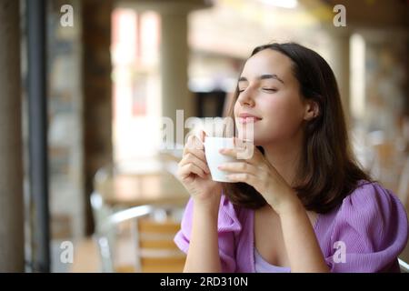 Eine Frau, die sich entspannt und nach Kaffee riecht, auf einer Barterrasse Stockfoto