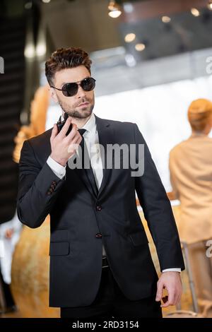 Leibwächter-Konzept, gutaussehender Mann in formeller Kleidung und Krawatte mit Walkie-Talkie, privater Sicherheitsdienst, schützt weibliche Klientin vor verschwommenem Hintergrund, verbinden Stockfoto