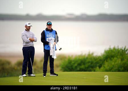 Patrick Cantlay (links) der USA und Caddie Joe LaCaza auf dem 17. Green mit Blick auf Hilbre Island und den River Dee während einer Übungsrunde vor den Open im Royal Liverpool, Wirral. Bilddatum: Dienstag, 18. Juli 2023. Stockfoto