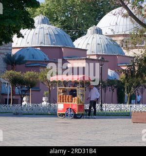 Hurrem Sultan Hammam türkisches Badehaus im Sultanahmet Park in Istanbul, Türkei, mit einem roten Verkaufswagen, in dem Simits auch türkische Bagels verkauft werden. Stockfoto