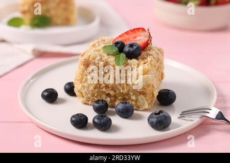 Ein Stück köstlicher Napoleonkuchen mit frischen Beeren auf einem rosa Holztisch, Nahaufnahme Stockfoto