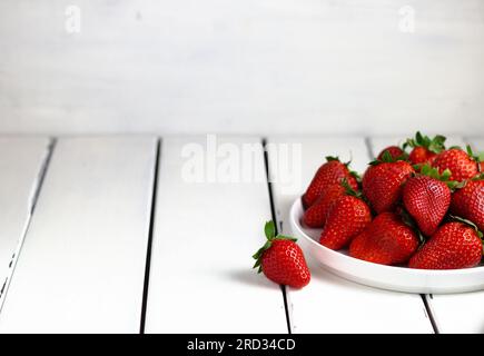 Haufen frischer Erdbeeren in Keramikschüssel auf rustikalem weißem Holzhintergrund. Stockfoto