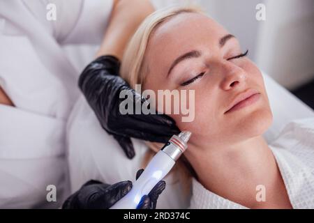 Die junge Frau liegt mit geschlossenen Augen, während sie die Gesichtshaut mit Feuchtigkeit versorgt. Die Blonde entspannt sich und genießt eine verjüngende Spa-Behandlung in einem Stockfoto