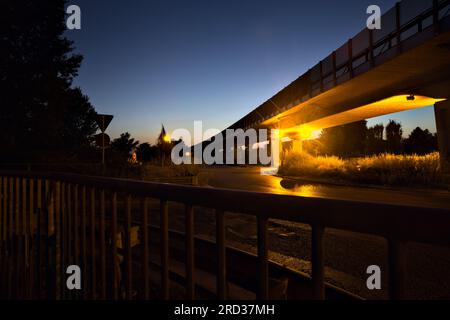 Kreisverkehr unter einem Viadukt in der italienischen Landschaft bei Nacht von einem Gehweg am Straßenrand aus gesehen Stockfoto