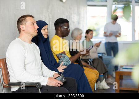Ein Mann mittleren Alters sitzt auf einem Stuhl in der Lobby des Büros und wartet auf einen Termin mit einem Spezialisten Stockfoto