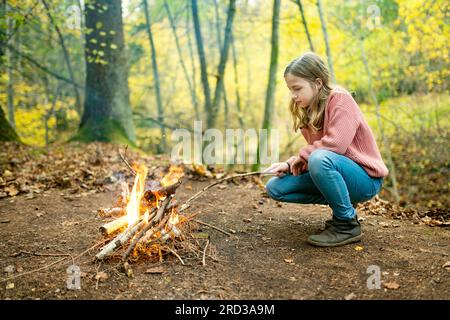 Cute jugendliche Mädchen rösten Marshmallows auf Stick am Lagerfeuer. Kind Spaß am Lagerfeuer. Camping mit Kindern im Herbst Wald. Familie Freizeit mit Stockfoto