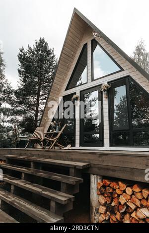 Ein modernes dreieckiges Haus mit A-Rahmen und großen Panoramafenstern im Wald für einen Wochenendausflug Stockfoto