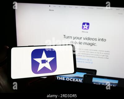 Person, die ein Smartphone mit dem Logo der Videobearbeitungssoftware iMovie (Apple Inc.) auf dem Bildschirm vor der Website hält. Konzentrieren Sie sich auf das Display des Telefons. Stockfoto