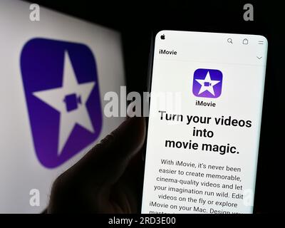 Person, die ein Mobiltelefon mit einer Website der Videobearbeitungssoftware iMovie (Apple Inc.) auf dem Bildschirm vor dem Logo hält. Konzentrieren Sie sich auf die Mitte des Telefondisplays. Stockfoto