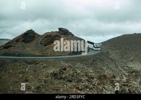 Ein Bus mit Touristen auf einer schmalen Straße im Timanfaya-Nationalpark, einer vulkanischen Umgebung auf Lanzarote, einer der Kanarischen Inseln, S. Stockfoto