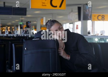 Müde Touristenfrau, die auf dem Gepäck schläft, während sie auf ihren Flug am Flughafenterminal wartete Stockfoto