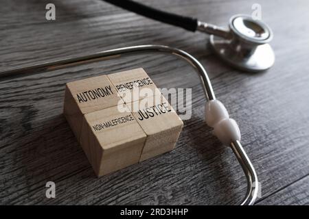 Stethoskop und Holzwürfel mit TEXTAUTONOMIE, VORTEIL, NICHT-MALEFICENCE und GERECHTIGKEIT. Die vier Säulen des medizinethischen Konzepts. Stockfoto