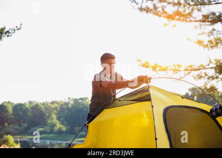 Ein hübscher weißer junger Mann baut ein Zelt in der Natur an einem sonnigen Sommertag auf. Camping. Stockfoto