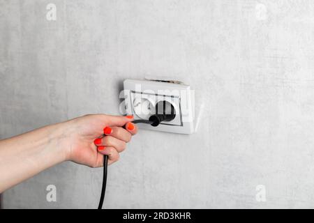 Das Mädchen zieht fälschlicherweise den Stecker aus der Steckdose und unterbricht die Steckdose. Stromschlaggefahr. Platz für Text kopieren Stockfoto